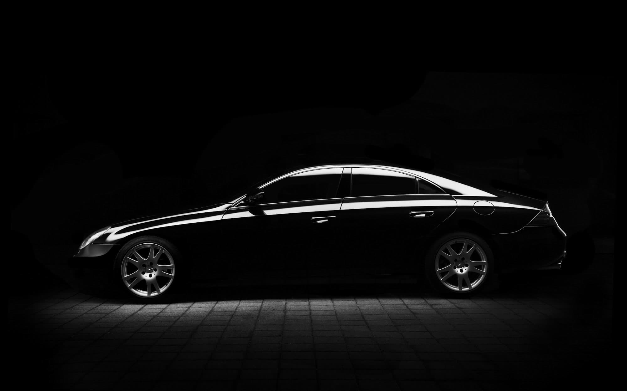 Black sedan lit from above in a dark studio