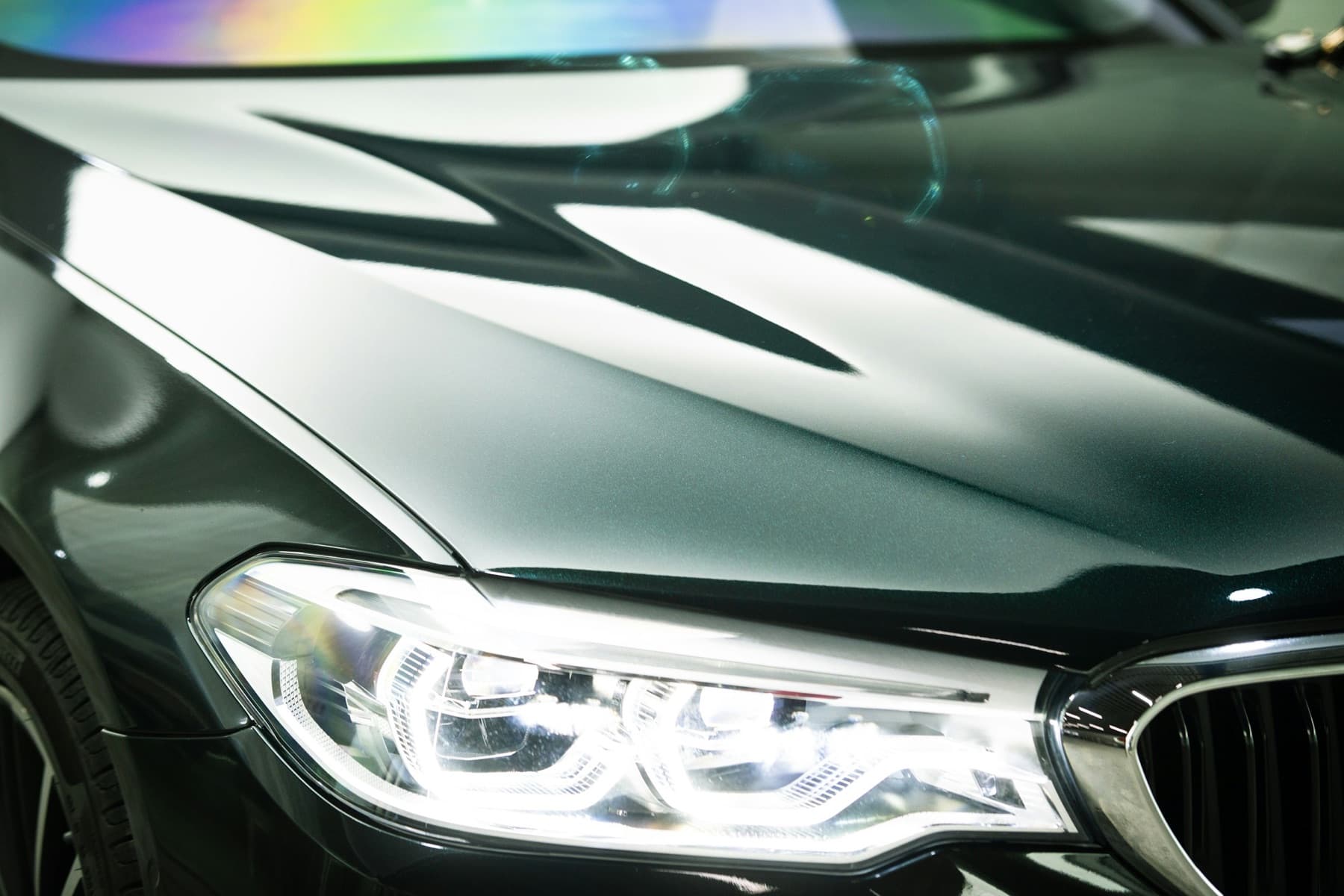 Close-up of a glossy dark car hood and headlight