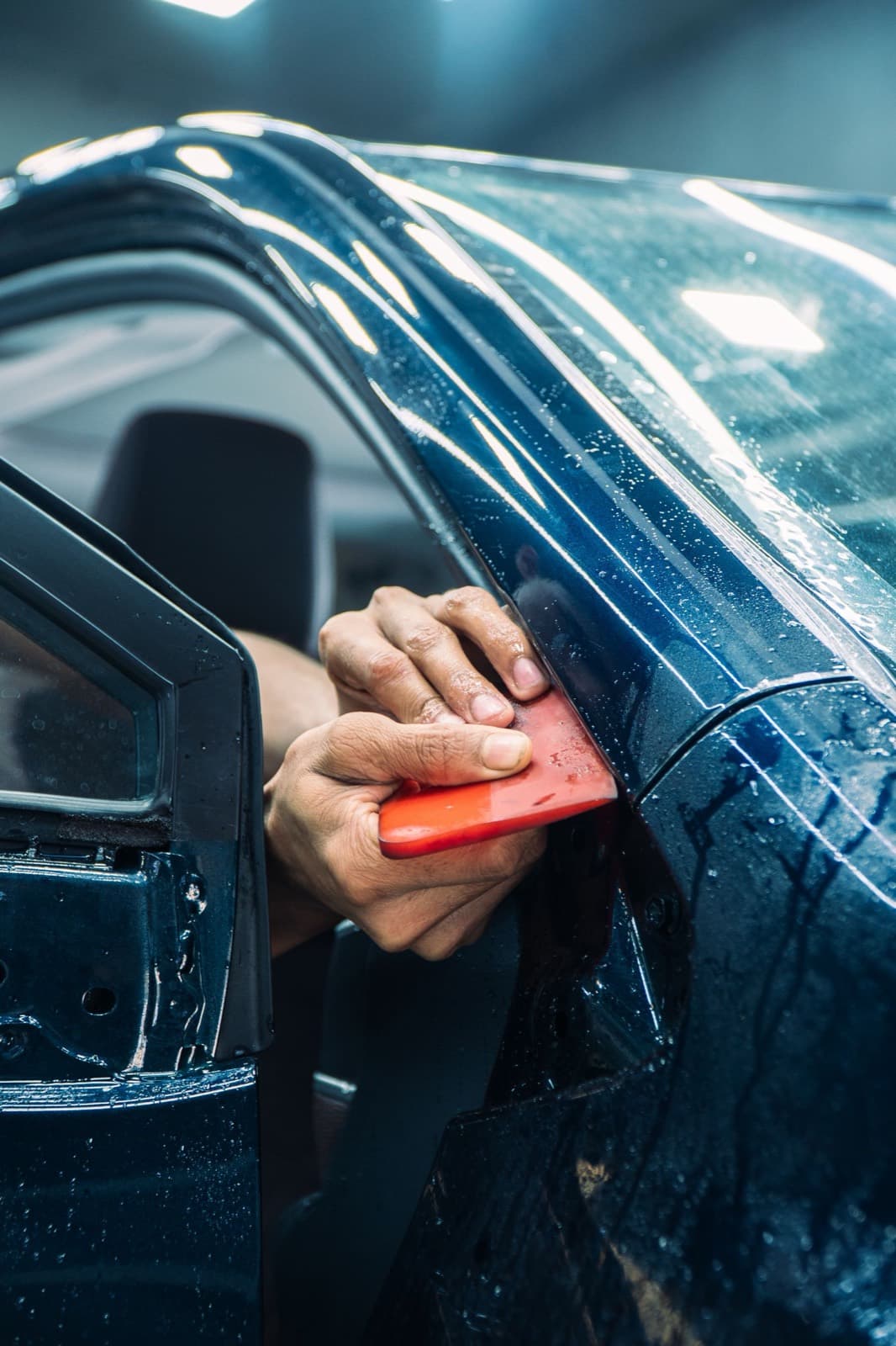 Technician pressing paint protection film onto a car door with a squeegee